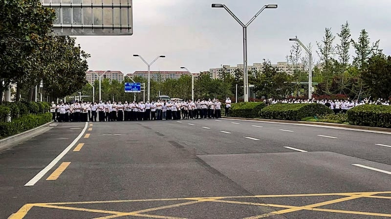 Plainclothes security officers stand on the road as people stage a protest at the entrance to a branch of China's central bank in Zhengzhou in central China's Henan Province on July 10, 2022. Credit: AP